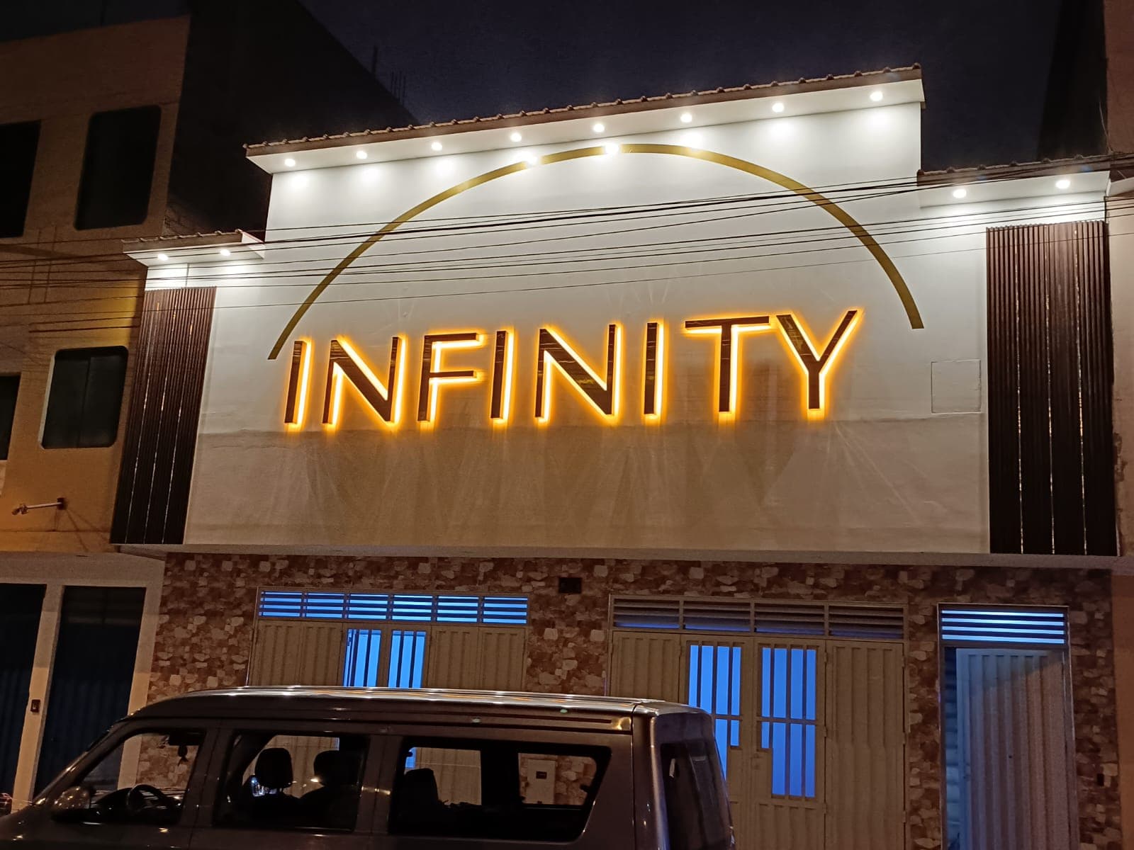 Fachada nocturna con letras INFINITY retroiluminadas bajo un arco dorado