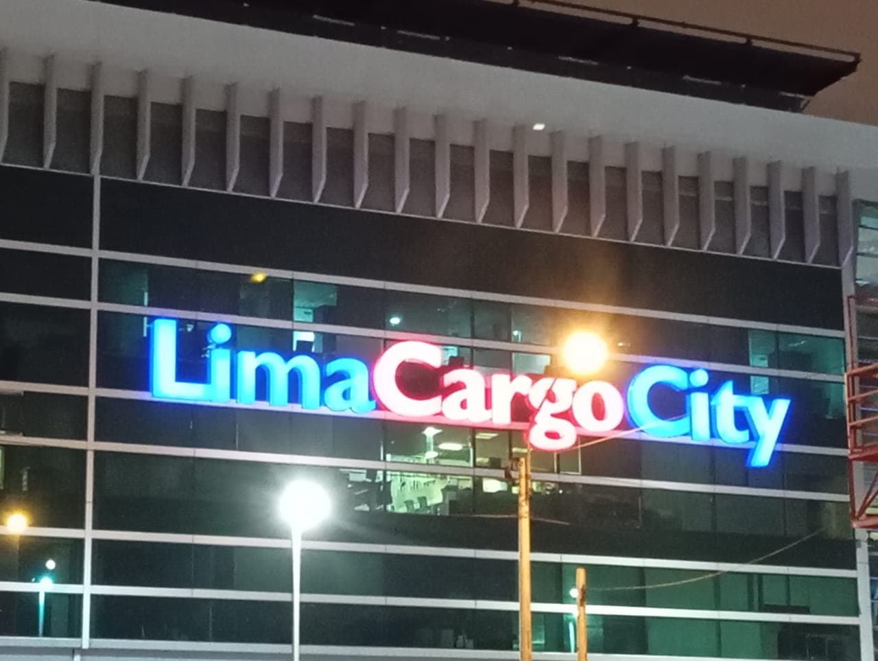 Letras luminosas Lima Cargo City en azul y rojo sobre una fachada de vidrio
